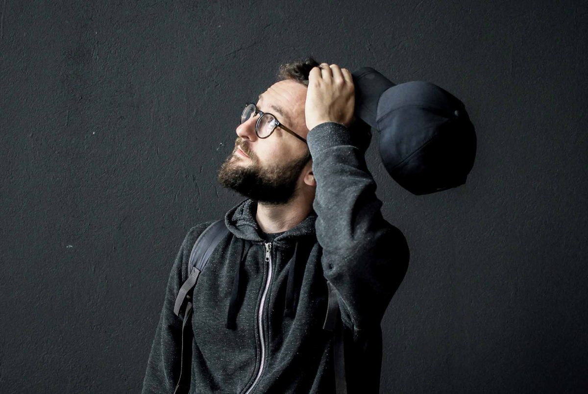 Young man looking up holding his hat