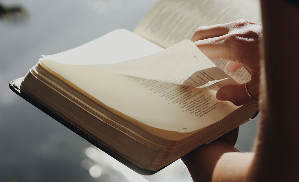 Woman holding open Bible with sparkling water in the background