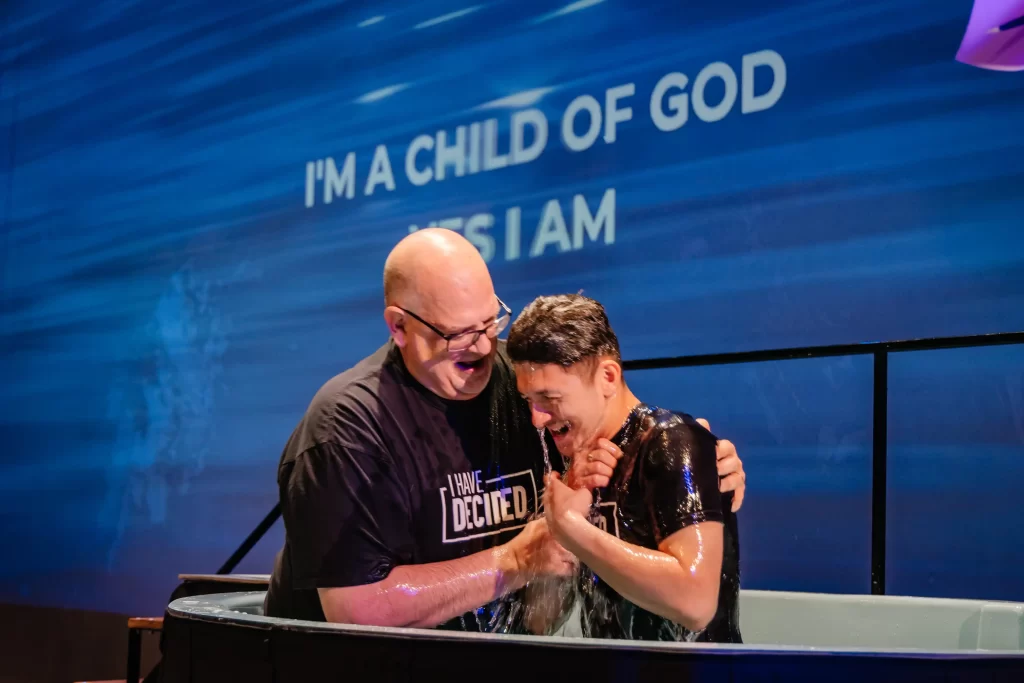 A pastor helping a male adult take the step of baptism at FAC Deerfoot